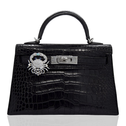 Black crocodile skin handbag with a silver clasp and brooch on a white background, collection-preview