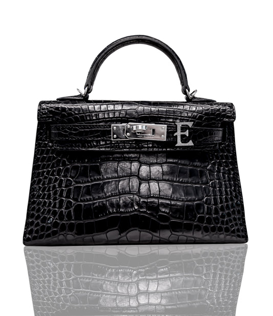 A black handbag with a crocodile pattern, featuring a metallic clasp and a leather handle, collection-preview.