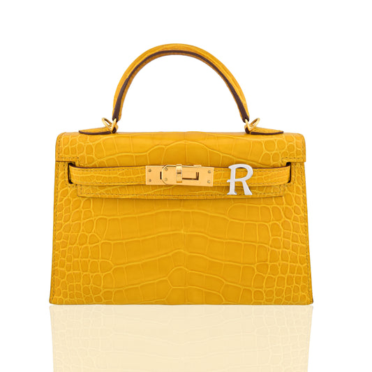 Yellow crocodile-patterned handbag with gold hardware and a white patch on a white background, collection-preview