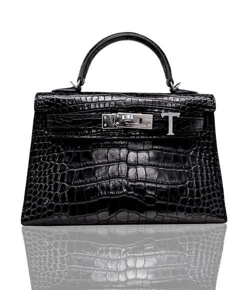 A black handbag with a crocodile pattern and a metallic 'T' closure, collection-preview.