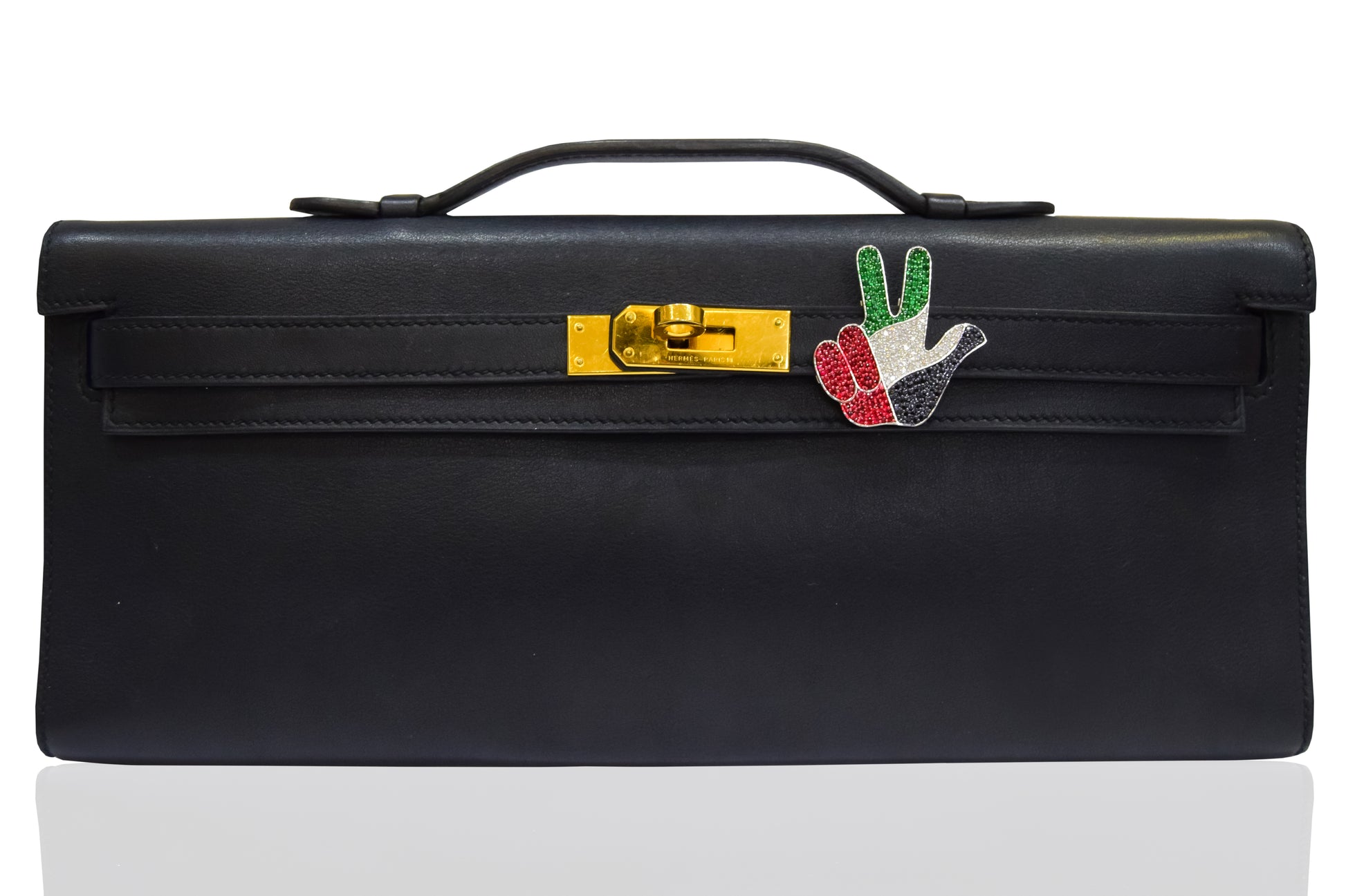 A black handbag with a metallic clasp and a decorative pin featuring geometric shapes and the colors red, green, and white. collection-preview.