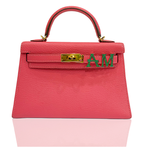 Pink handbag with gold clasp and green letters on a white background, collection-preview