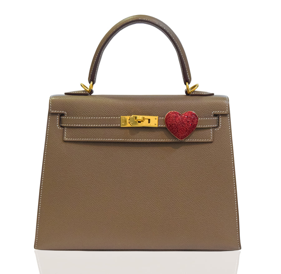 Brown handbag with a gold clasp and red heart charm on a white background, collection-preview