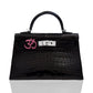 Black crocodile-patterned handbag with a pink and silver emblem on a white background, collection-preview