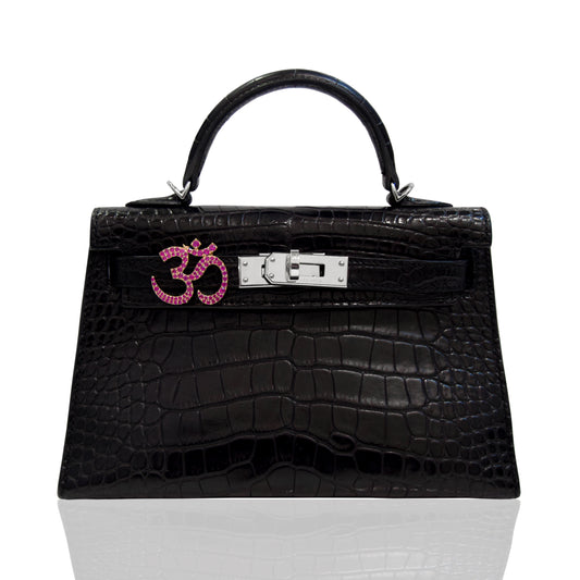 Black crocodile-patterned handbag with a pink and silver emblem on a white background, collection-preview
