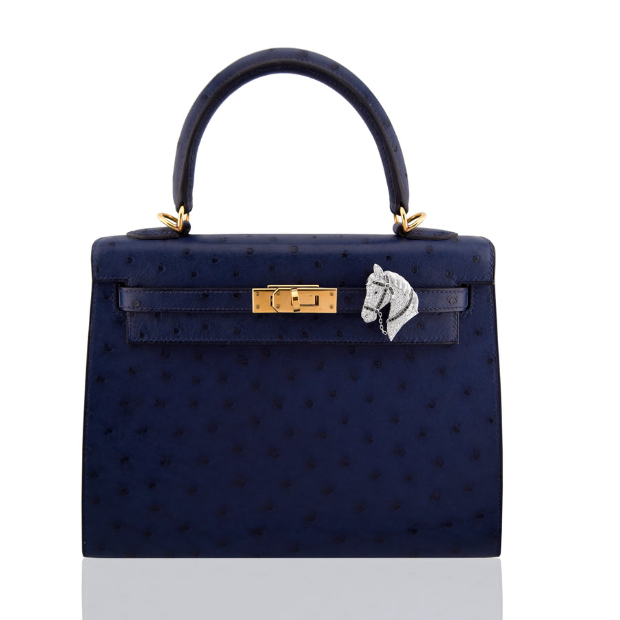 Navy blue handbag with gold hardware and a horse emblem on a white background, collection-preview