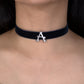 Black choker necklace with a silver 'A' pendant on a person wearing a gold garment.