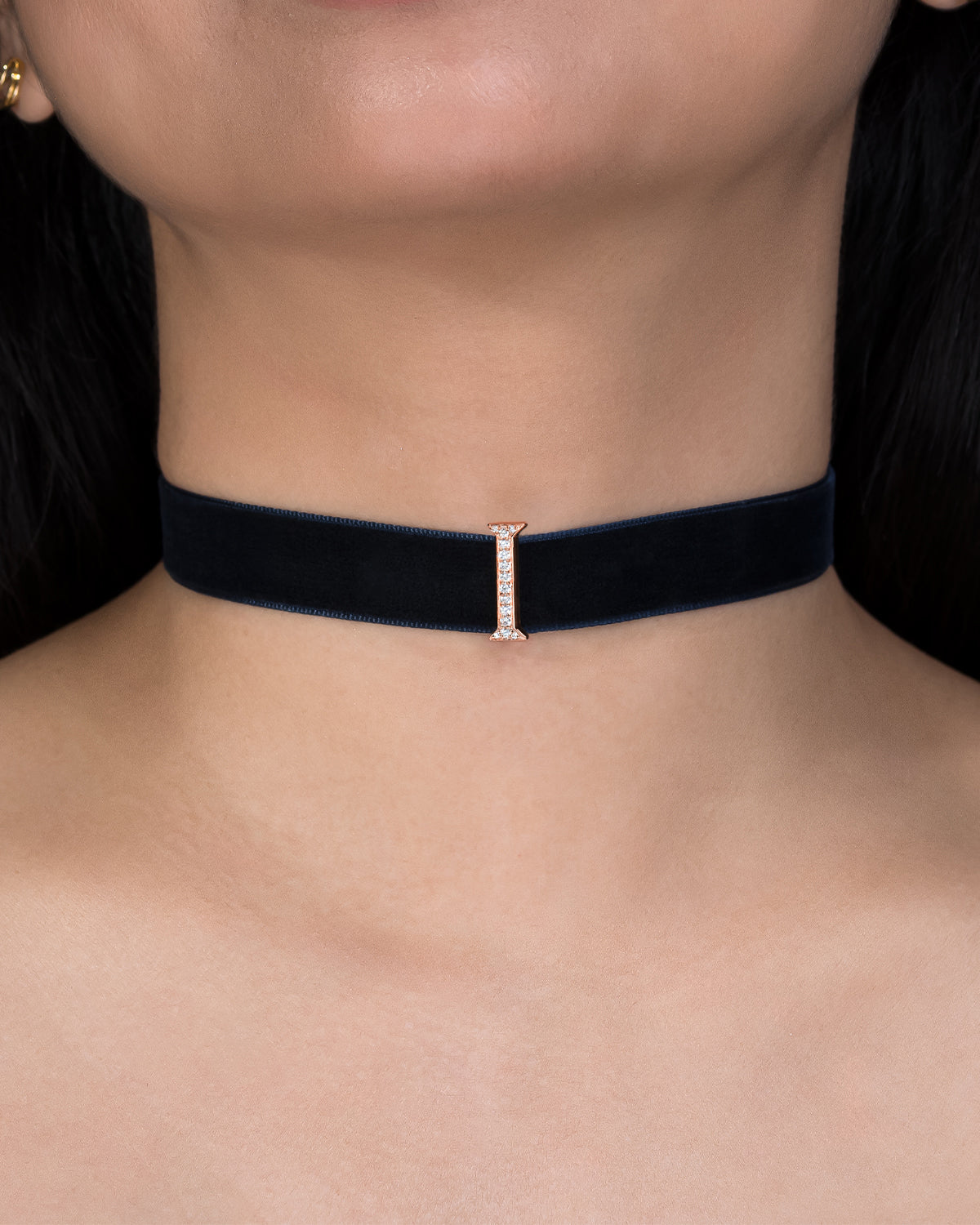 Black choker with a small diamond clasp on a person's neck against a black background