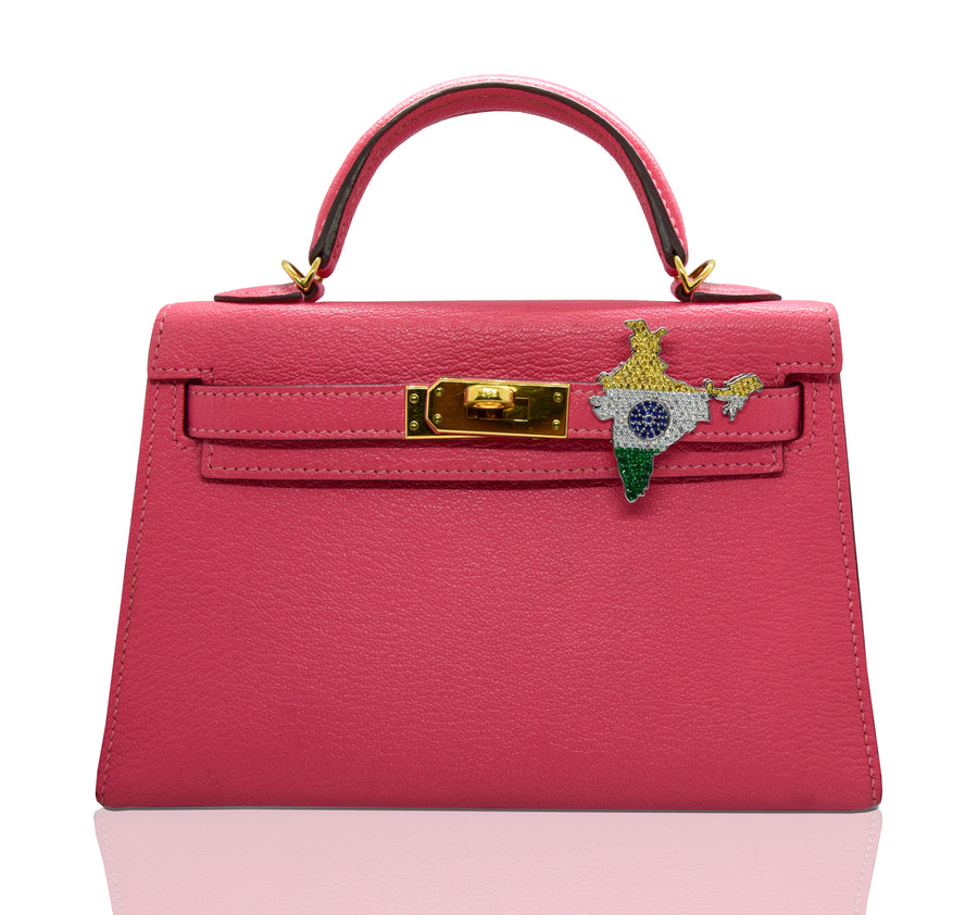 A pink handbag with a brooch featuring a floral design and the India flag colors attached to the clasp, collection-preview.