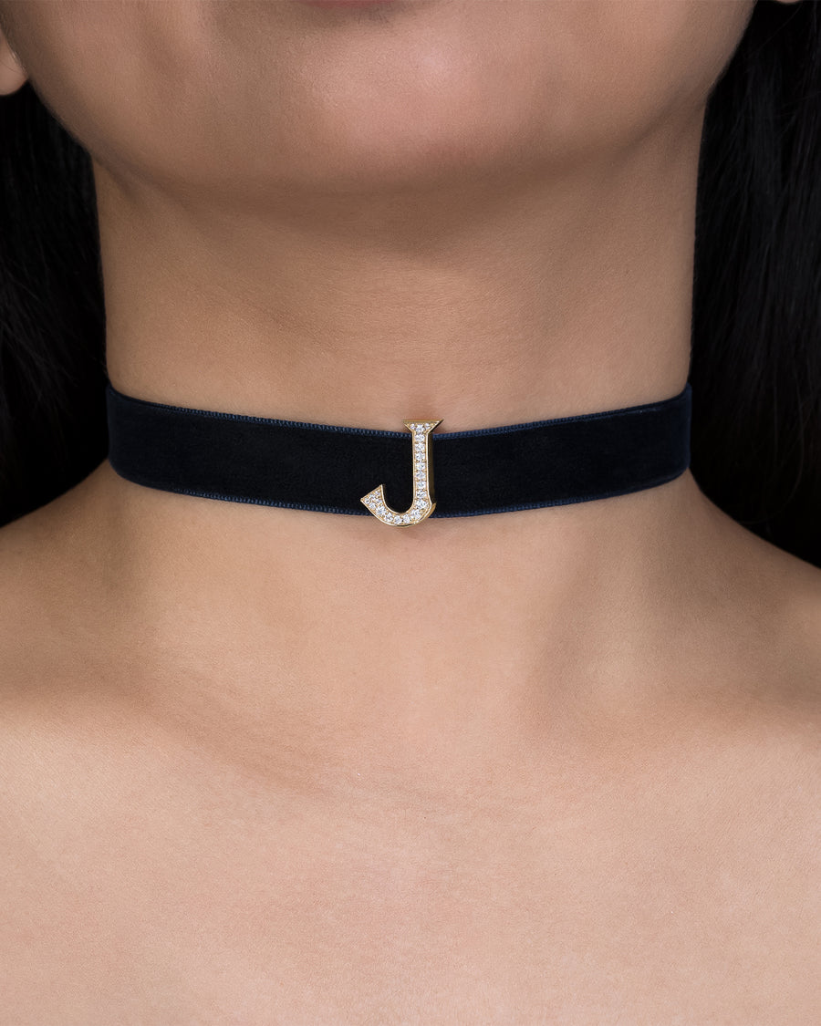 Black choker necklace with a gold 'J' pendant on a person's neck.