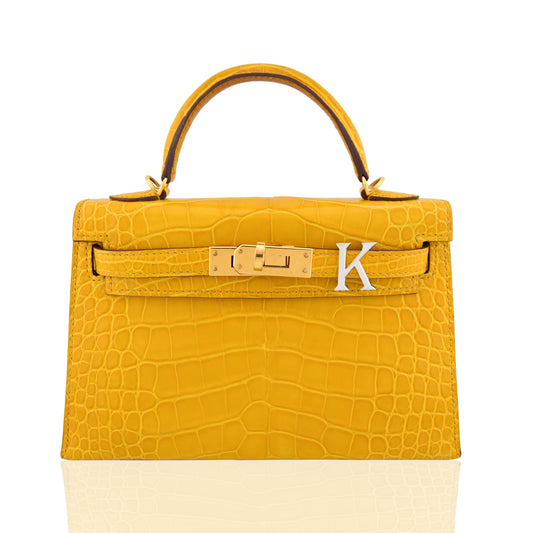 Yellow crocodile-patterned handbag with gold hardware and a silver 'K' on a white background, collection-preview