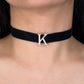 Black velvet choker with a silver 'K' pendant on a person's neck.