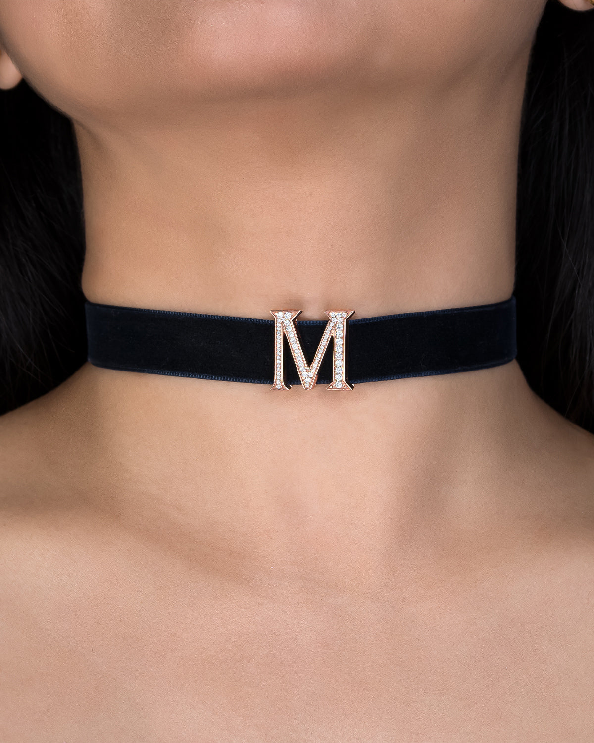 Black choker with a gold 'M' pendant on a person's neck