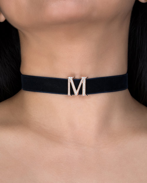 Black choker with a gold 'M' pendant on a person's neck