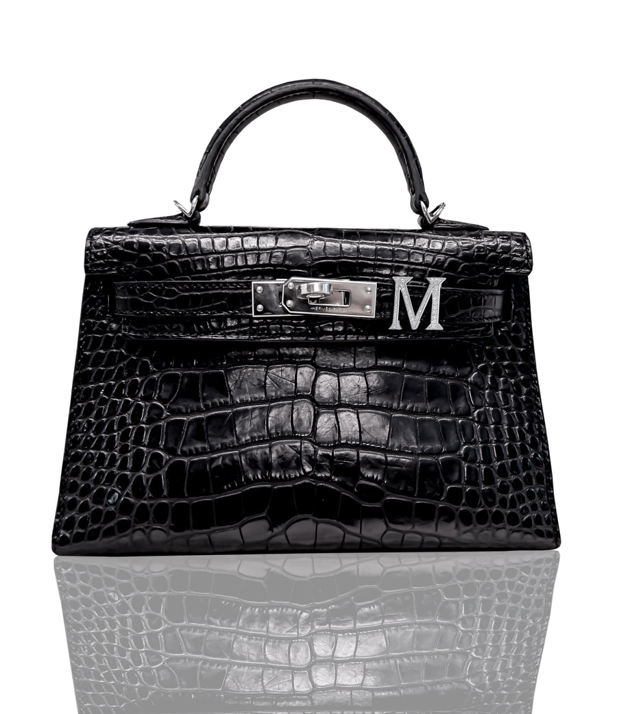 A black crocodile patterned handbag with a silver 'M' initial piece attached to the front, collection-preview.
