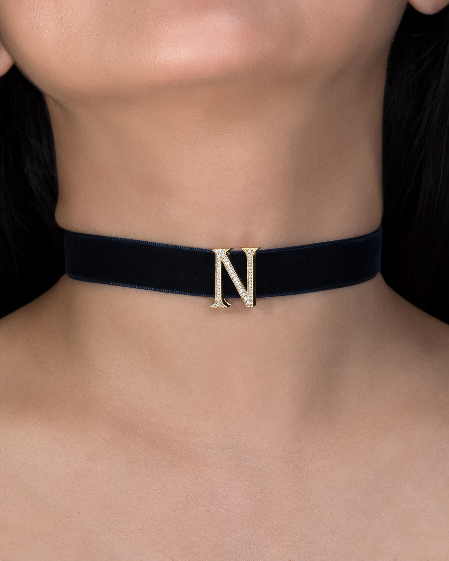 Black choker necklace with a gold letter 'N' on a person's neck