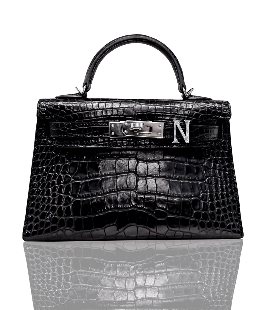 A black handbag with a crocodile pattern and a metallic letter 'N' emblem on the front, collection-preview.