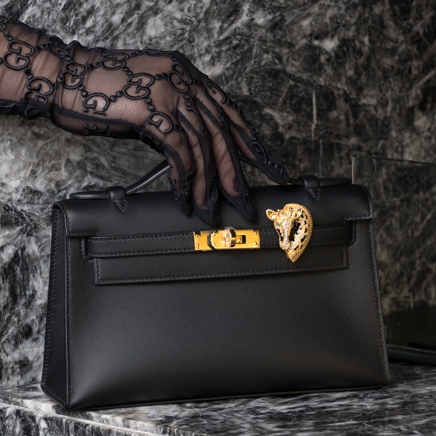 Black handbag with gold clasp held by a gloved hand against a marble background