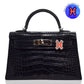 Black crocodile-patterned handbag with a distinctive clasp on a white background, collection-preview