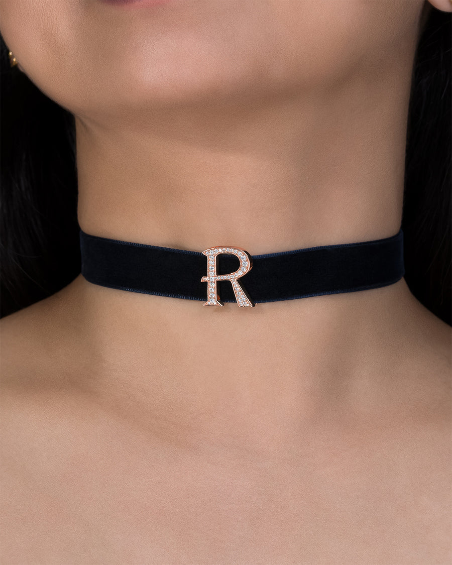 Navy blue choker with a rose gold 'R' on a person's neck