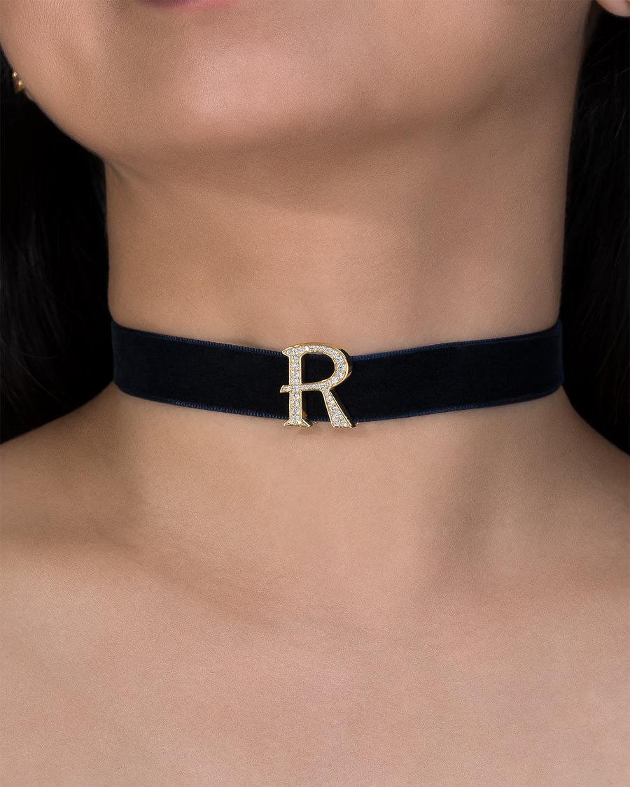 Black choker with a gold letter 'R' on a person's neck
