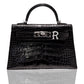 A black handbag with a crocodile pattern and a silver brooch with the letter 'R' attached to it, collection-preview.