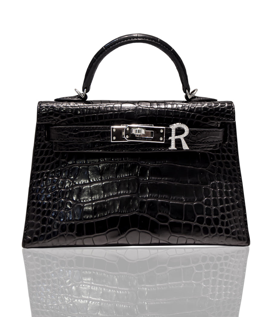 A black handbag with a crocodile pattern and a silver brooch with the letter 'R' attached to it, collection-preview.