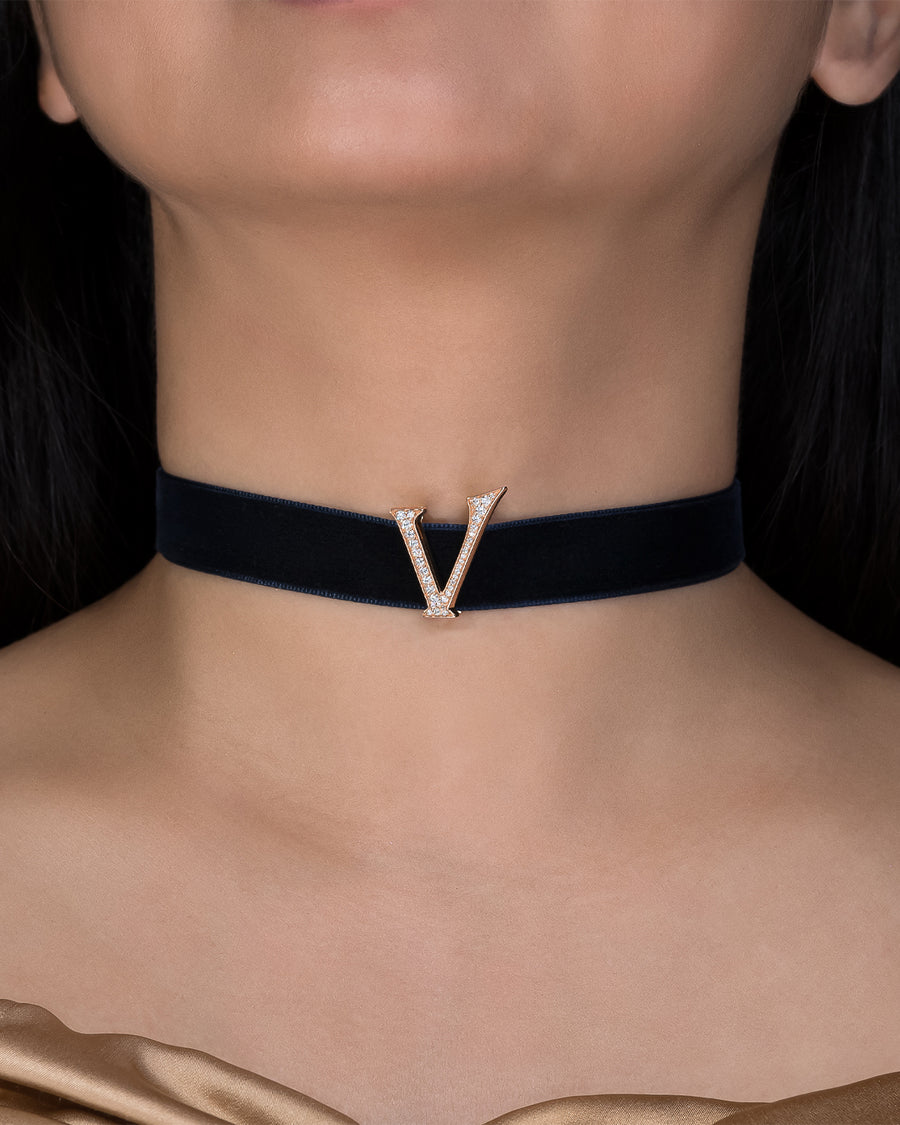 Black choker with a gold 'V' pendant on a person's neck against a dark background