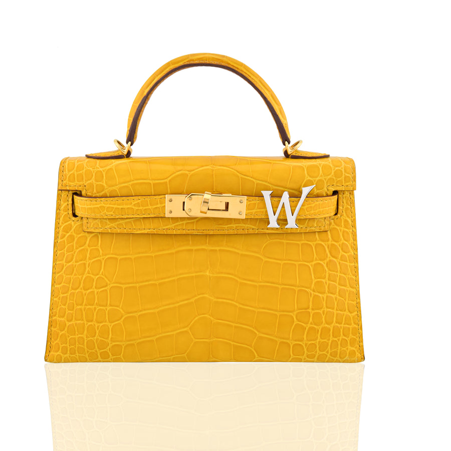 Yellow crocodile-patterned handbag with a gold clasp and white letter 'W' on a white background, collection-preview